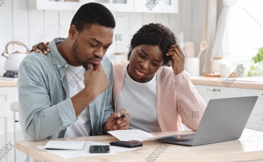 pay off credit card debt faster: American family sitting at kitchen table stressed looking at credit card bills and planning debt payoff strategy with calculator
